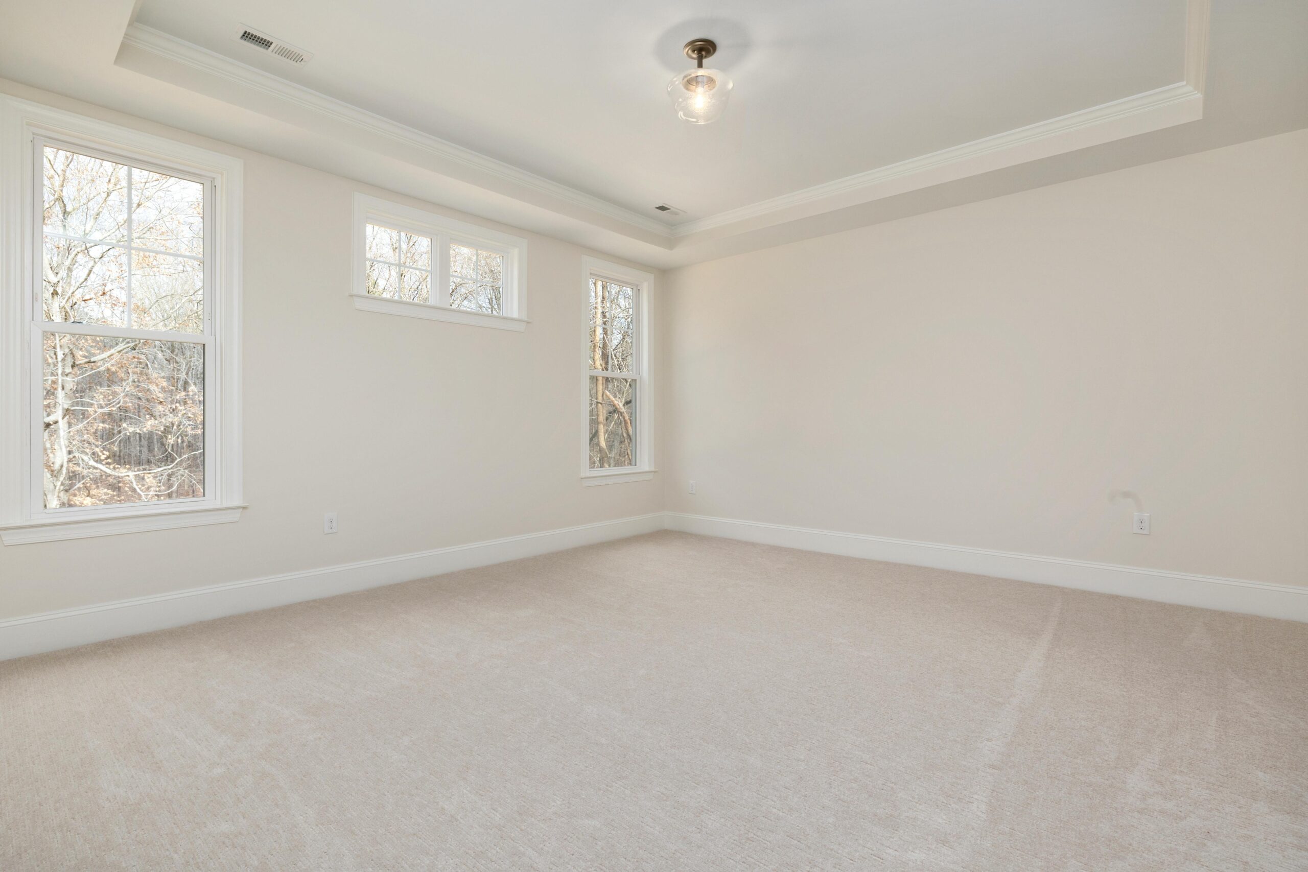 Bright empty room with large windows, neutral walls, and soft carpet flooring.