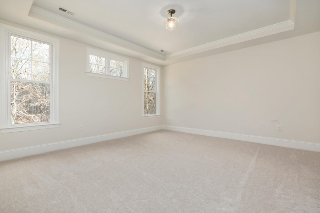 Bright empty room with large windows, neutral walls, and soft carpet flooring.