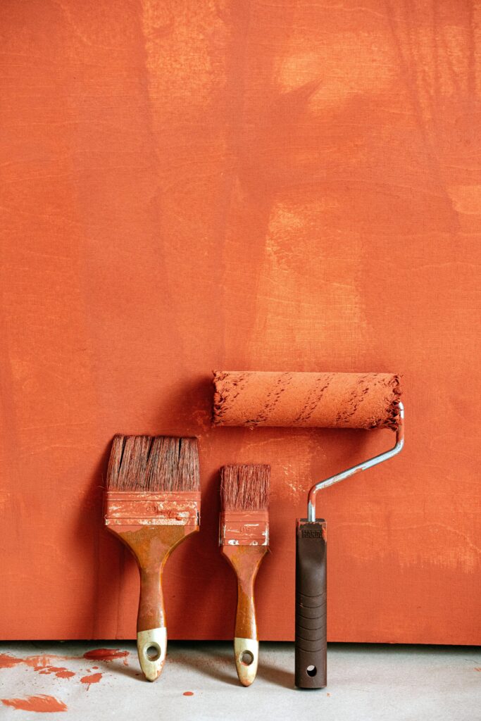 Close-up of paintbrushes and roller with orange backdrop, perfect for home renovation concepts.