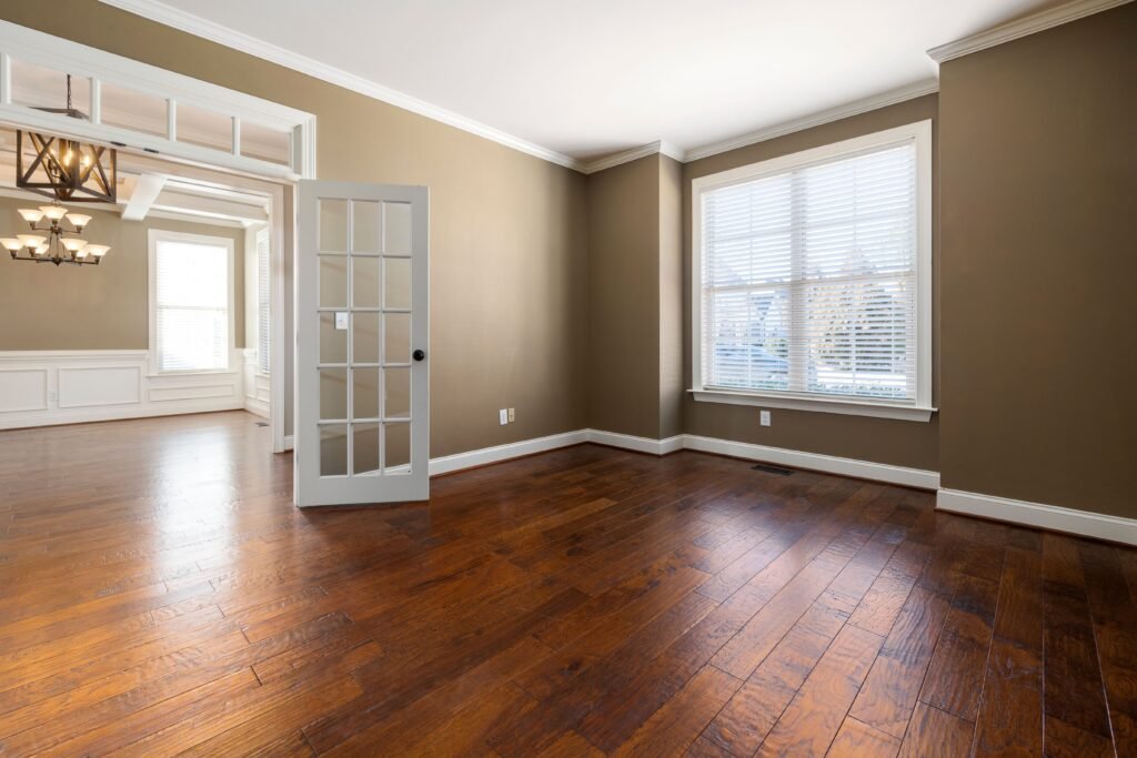 Bright and empty room with hardwood flooring, large windows, and elegant lighting.
