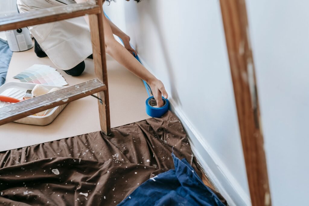 Woman preparing room for painting with adhesive tape and tools; home renovation project.